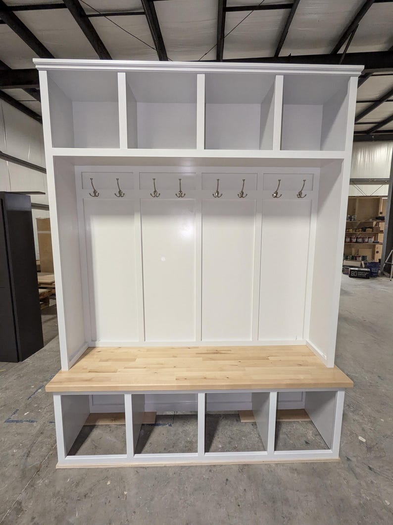May include: White wooden entryway bench with a built-in cubby storage system and a top shelf. The bench has a light wood top and a white painted finish.