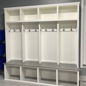 May include: White wooden entryway bench with a gray top and three cubbies. The bench has a row of hooks on the top for hanging coats, bags, or hats.