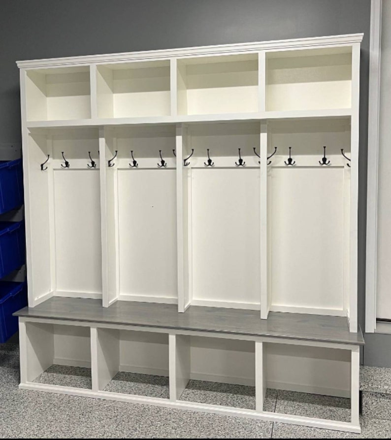 May include: White wooden entryway bench with a gray top and three cubbies. The bench has a row of hooks on the top for hanging coats, bags, or hats.