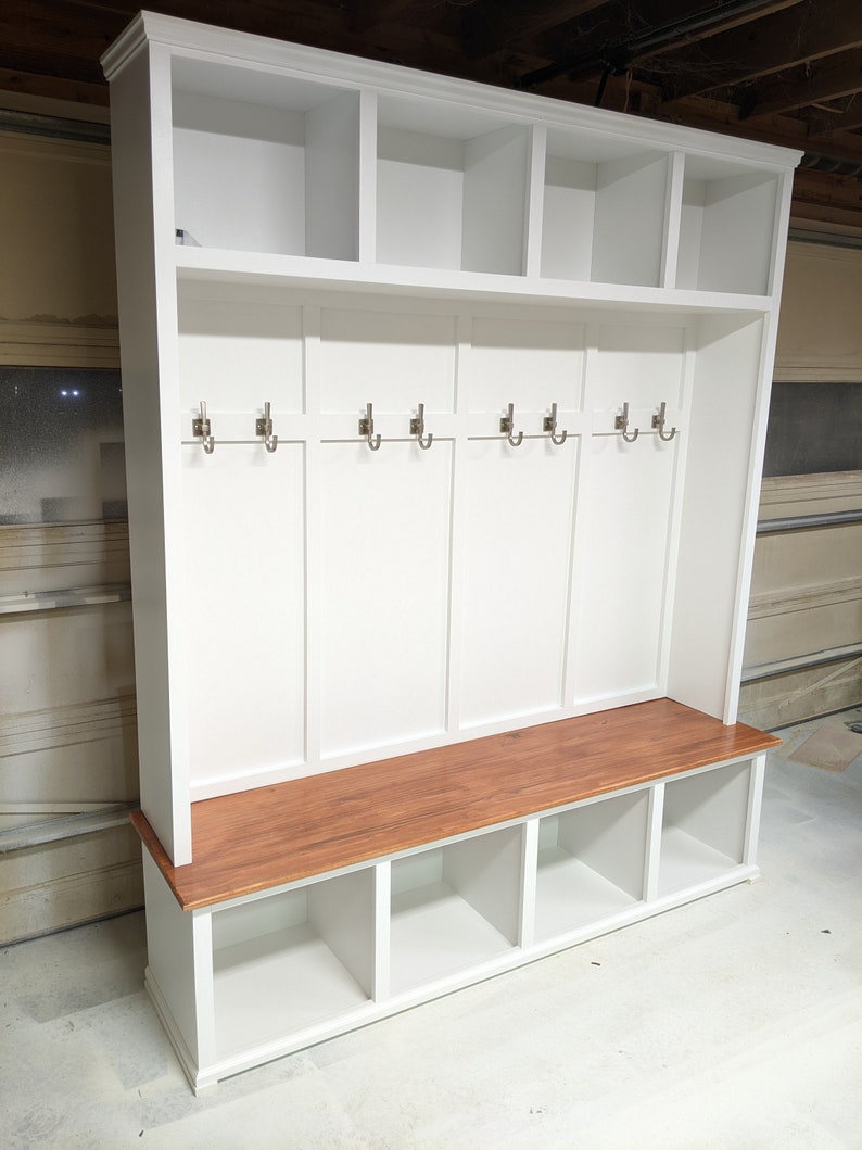 May include: White wooden entryway bench with a brown wood top, six hooks, and three cubbies below the bench.