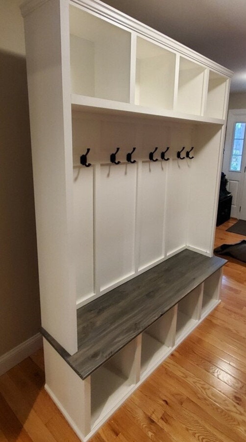 May include: White wooden entryway bench with a gray wood top, five hooks, and three storage cubbies. The bench is against a wall with wood flooring.