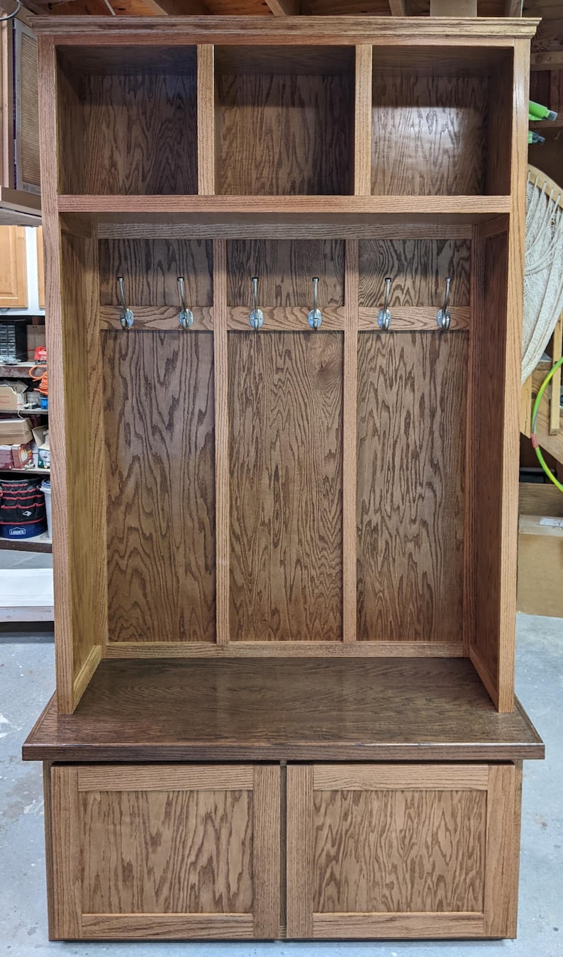 May include: A wooden entryway bench with a coat rack and storage compartments. The bench has a dark brown stain and features two drawers with a raised panel design. The coat rack has five hooks.