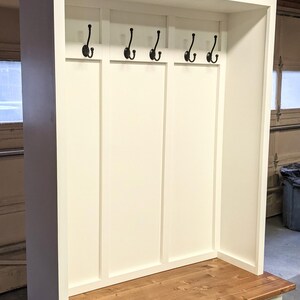 May include: White wooden entryway bench with a brown wood top, three drawers, and a shelf with hooks.