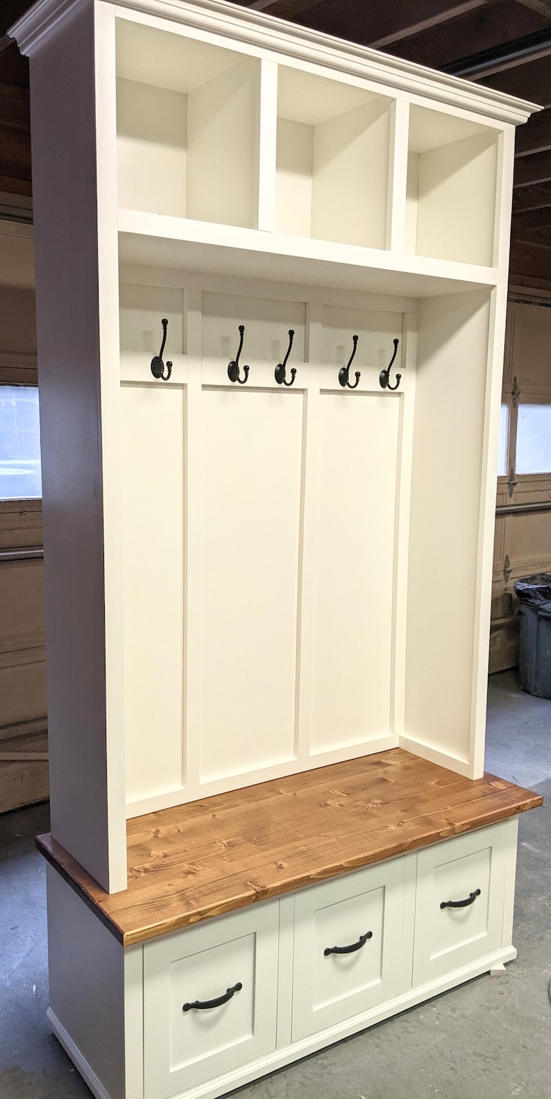 May include: White wooden entryway bench with a brown wood top, three drawers, and a shelf with hooks.