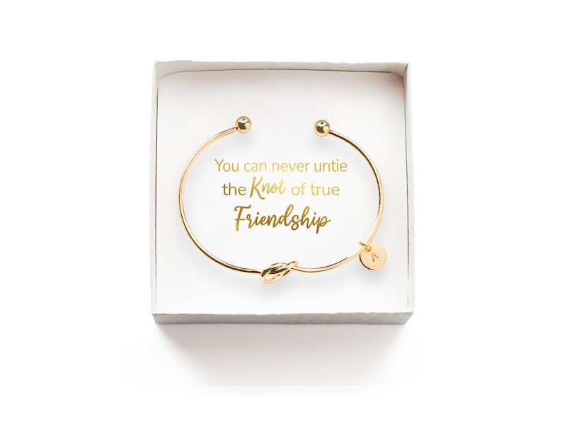 Puede incluir: Pulsera de amistad dorada con un dise&ntilde;o de nudo y un dije que dice "You can never untie the knot of true friendship". La pulsera est&aacute; en una caja blanca.