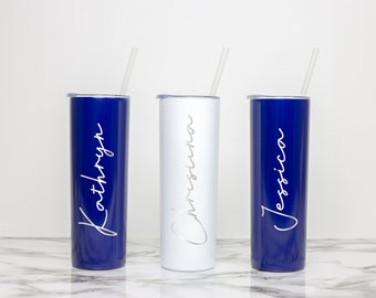 May include: Three stainless steel tumblers with straws. The tumblers are blue, white, and blue. The names "Kathryn", "Christina", and "Jessica" are written on the tumblers in white.
