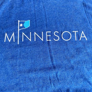 May include: A blue t-shirt with a white graphic of a flag and the word "MINNESOTA" printed on the front.