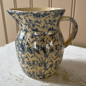 May include: A vintage blue and cream ceramic pitcher with a speckled glaze. The pitcher has a rounded body and a handle.