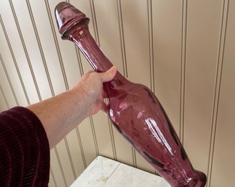 May include: A tall, purple glass bottle with a unique, bulbous top. The bottle has a swirling, marbled pattern and a clear, glossy finish.