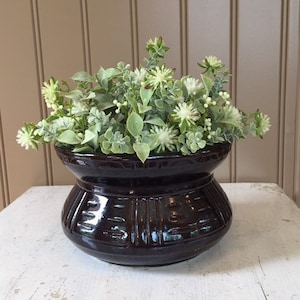 May include: A dark brown ceramic planter with a wide base and a narrow neck, filled with a green and white leafy plant.