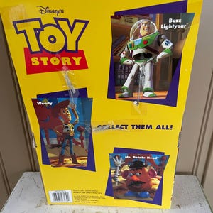 May include: Yellow Toy Story box featuring Woody, Buzz Lightyear, and Mr. Potato Head. The box has the Disney's Toy Story logo and the text "COLLECT THEM ALL!" The box is on a white surface.