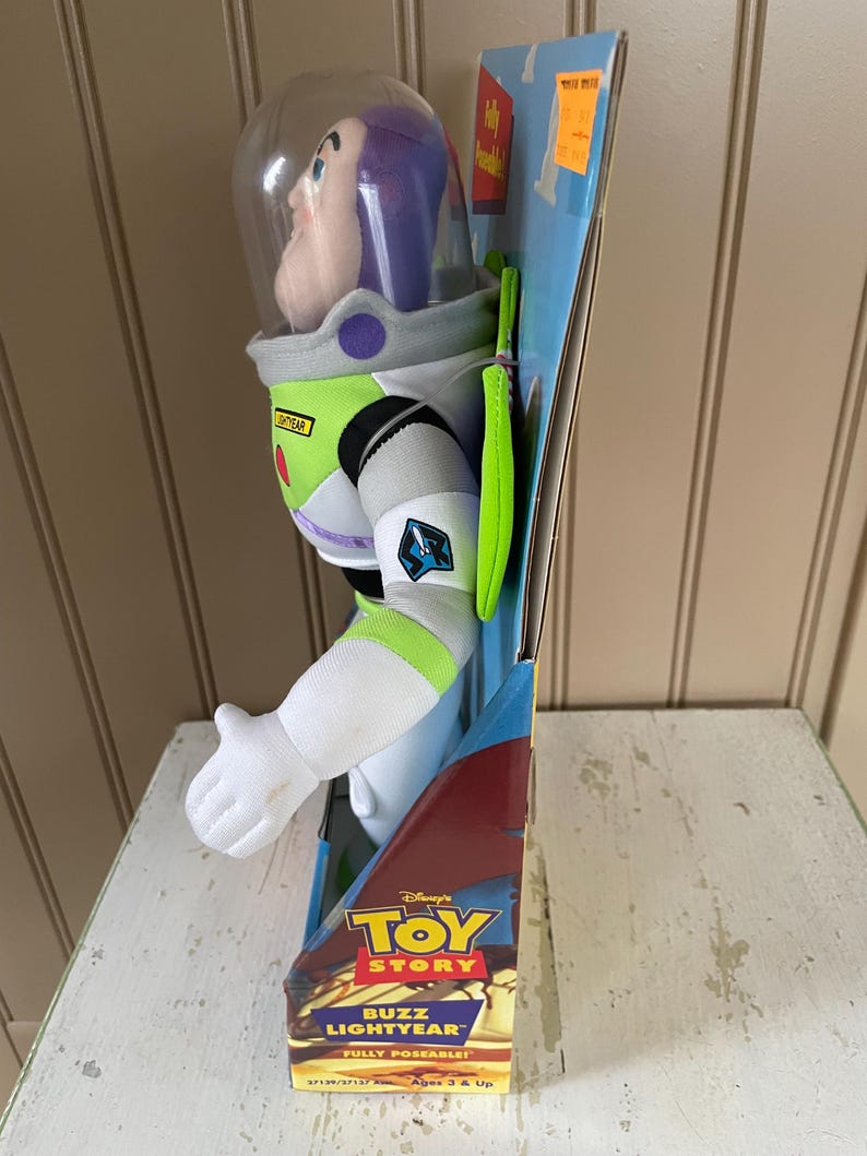 May include: A Buzz Lightyear plush toy from Disney's Toy Story, fully poseable. The toy is in its original packaging, featuring a clear helmet, white spacesuit with green and purple accents. The packaging includes the text "BUZZ LIGHTYEAR" and "FULLY POSEABLE!"