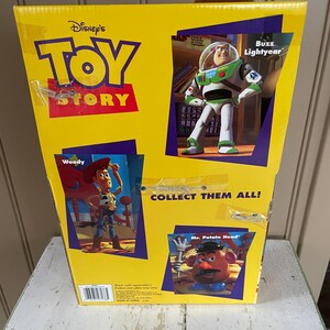 May include: Yellow Disney Toy Story box featuring Woody, Buzz Lightyear, and Mr. Potato Head. The box has the words "Toy Story" in red and blue. The box also says "Collect Them All!"