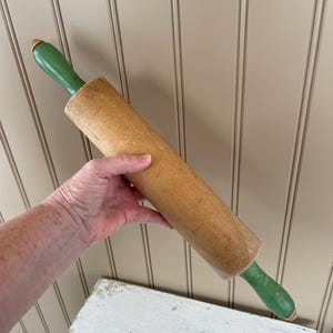 May include: A wooden rolling pin with green handles. The rolling pin is approximately 18 inches long.