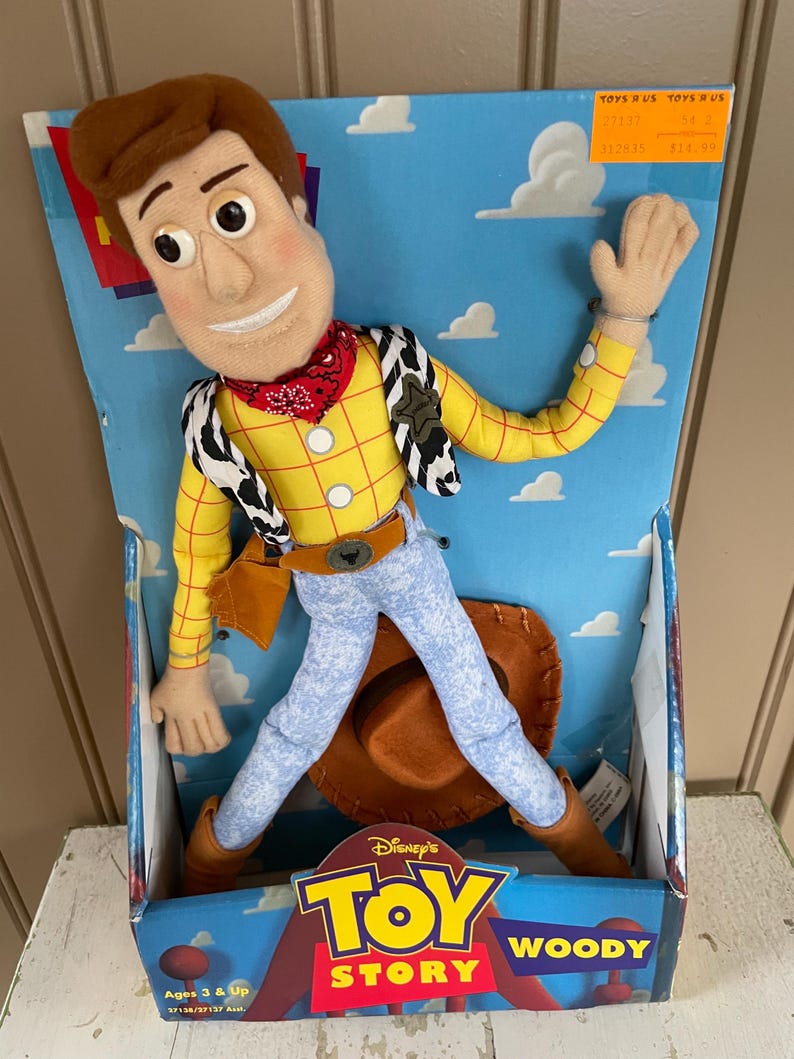 May include: A Woody doll from Disney's Toy Story, in its original box. The doll is wearing a yellow shirt, blue jeans, a red bandana, and a cowboy hat. The box has the Toy Story logo and the words "Woody".
