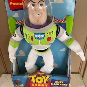 May include: Buzz Lightyear plush doll from Disney's Toy Story, in its original box. The doll features a white and green spacesuit, a clear helmet, and the words "Buzz Lightyear" on the box. The box also has the Toy Story logo.