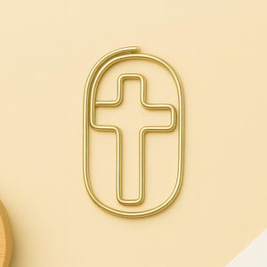 Peut inclure: Un trombone doré en forme de croix, inséré dans un cadre ovale. Le trombone est placé sur un fond jaune clair. Le design est simple et élégant, adapté à un usage de bureau ou religieux.