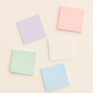 May include: Five pastel-coloured square sticky notes in shades of lavender, pink, white, mint green, and light blue. The sticky notes are arranged on a cream-coloured surface. Suitable for office or school use.