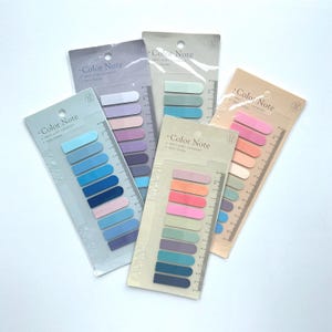 Puede incluir: Cinco paquetes de marcadores de página adhesivos en varios colores pastel. Cada paquete contiene diez marcadores y una regla impresa en el embalaje. El texto "Color Note" está impreso en cada paquete.