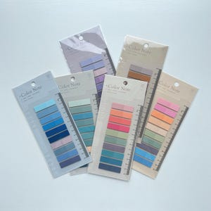 May include: Several packs of sticky notes in various color palettes. Each pack contains ten notes and features a ruler-like design on the side. The packaging reads "Color Note". The color schemes include blues, greens, pinks, and oranges.