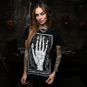 May include: A black t-shirt featuring a white graphic print of a hand with flames and the text "Wheel of Fortune".