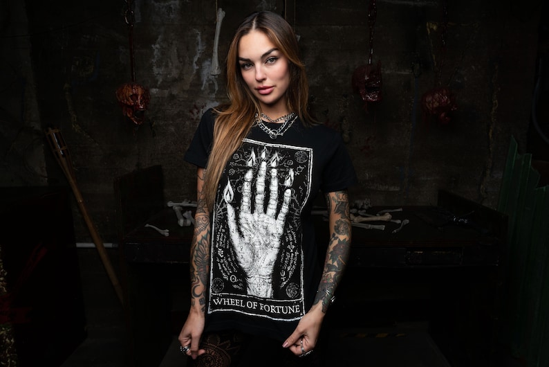 May include: A black t-shirt featuring a white graphic print of a hand with flames and the text "Wheel of Fortune".