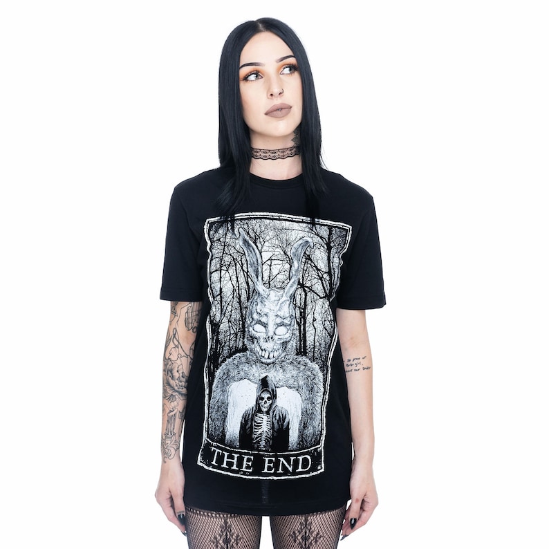 K&ouml;nnte beinhalten: Schwarzes T-Shirt mit einem wei&szlig;en Grafikdruck eines Kaninchens mit Maske und einer Kapuzenfigur mit einem Skelett darunter. Die Grafik ist in einem schwarzen Rechteck mit dem Text "THE END" darunter gerahmt.