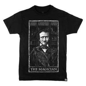 May include: Black t-shirt featuring a white graphic of Edgar Allan Poe with a raven on his shoulder. The graphic is framed in a white rectangle with the text "THE MAGICIAN" at the bottom.