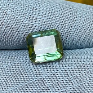May include: A green gemstone with a square cut and a slightly cloudy appearance.