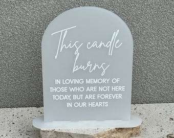 May include: A white acrylic sign with rounded edges and a message that reads "This candle burns in loving memory of those who are not here today, but are forever in our hearts".