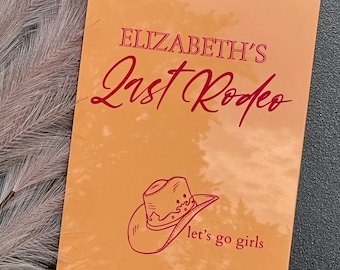 May include: A peach-colored card with the text "Elizabeth's Last Rodeo" in red. A red line drawing of a cowboy hat is below the text with the words "let's go girls" underneath.