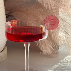 May include: A clear glass with a red drink and a pink paper tag that says "Annie's Hens" with a cocktail glass icon.