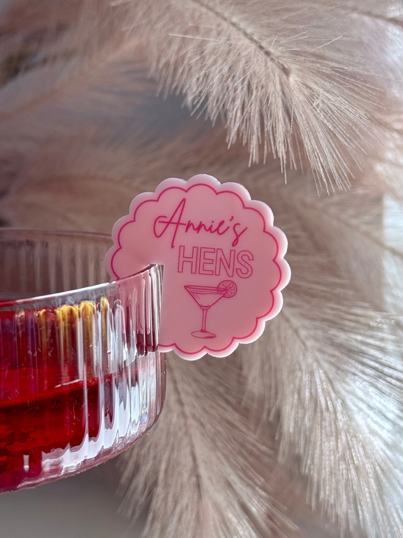 May include: Pink and white circular drink marker with the text "Annie's Hens" and a pink cocktail glass icon.