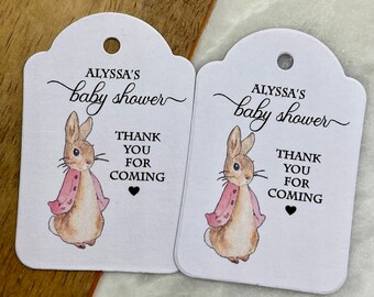 May include: Two white favor tags with a Peter Rabbit illustration. The tags are scalloped and have the text "Alyssa's baby shower" and "Thank you for coming" with a small heart.