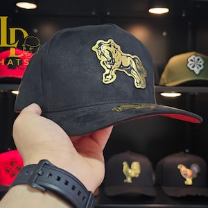 May include: Black suede baseball cap with a gold horse emblem. The cap has a red brim and a curved visor. The hat is part of a collection of hats with various emblems.