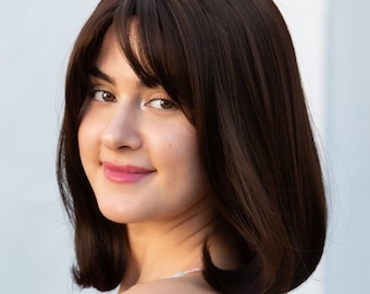 May include: A woman with shoulder-length brown hair styled in a bob with a side parting and bangs. She is wearing a light pink and blue floral print off-the-shoulder top.