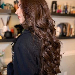 Pu&ograve; includere: Una donna con capelli lunghi, castani e ondulati. Indossa una giacca nera.