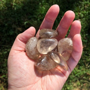 Op de afbeelding: Een verzameling van zes getrommelde rookkwartsstenen in verschillende maten en vormen. De stenen zijn lichtbruin van kleur en hebben een doorschijnende uitstraling.