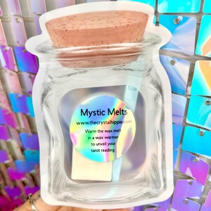 K&ouml;nnte beinhalten: Eine transparente, gl&auml;serne Verpackung mit einem Wachsschmelz und einem Korken. Die Verpackung tr&auml;gt ein Etikett mit der Aufschrift "Mystic Melts" und der Website-Adresse. Der Text auf dem Etikett besagt auch, dass man den Wachsschmelz in einem Wachsw&auml;rmer erw&auml;rmen soll, um Ihre Tarot-Lesung zu enth&uuml;llen.