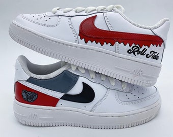 Könnte beinhalten: Weiße Lederschuhe mit roten und schwarzen Nike-Swoosh-Logos. Der rechte Schuh hat einen roten Swoosh mit einem gezackten Rand und den Text "Roll Tide" in Schwarz. Der linke Schuh hat einen schwarzen Swoosh und ein rotes und graues Panel mit einer grauen Elefantengrafik.