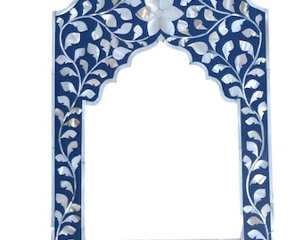 May include: A decorative blue frame with a floral and leaf design. The frame is adorned with white mother-of-pearl inlays, creating a contrasting pattern. The frame has an arched top and is suitable for a mirror or artwork.
