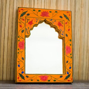 May include: A decorative orange mirror with a floral design painted around the frame. The mirror has an arched opening and is painted with green, red, and blue flowers.