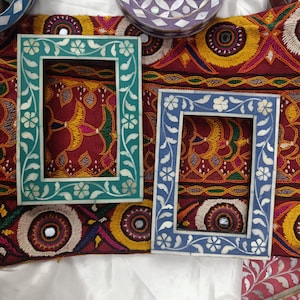 Könnte beinhalten: Zwei verzierte Bilderrahmen mit aufwendigen floralen Designs. Die Rahmen sind aus weißem Knocheninlay mit blauen und türkisfarbenen Akzenten. Die Rahmen sind vor einem bunten Stoffhintergrund platziert.
