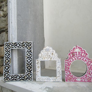 May include: Three decorative picture frames made of wood and inlaid with mother of pearl. The frames are in different styles and colors, including black, white, and pink.