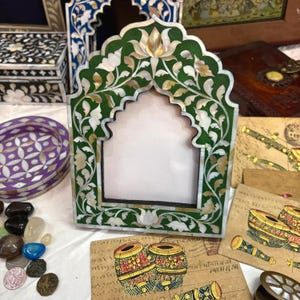 May include: A green picture frame with a white and gold floral design. The frame is made of wood and has a mother-of-pearl inlay. The frame is in the shape of an archway.