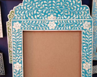 May include: A turquoise blue picture frame with a white floral design. The frame is made of mother of pearl and has a rectangular shape.