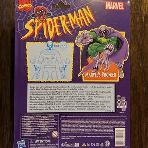 May include: Back of a Marvel Comics Spider-Man action figure package featuring the Prowler. The package is purple and features a cartoon image of the Prowler in his green and purple suit. The text on the package reads "Marvel's Prowler".