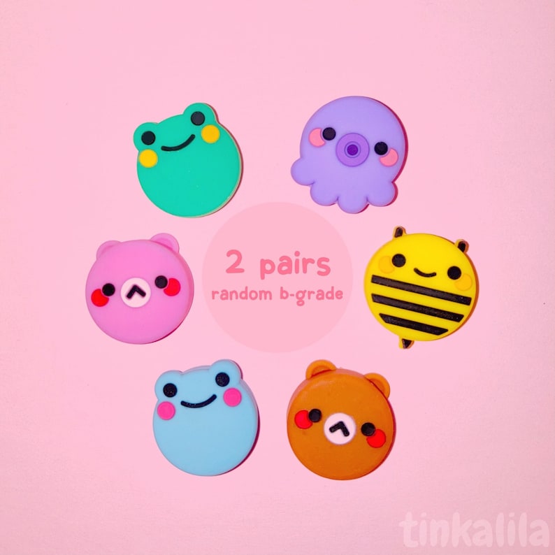Pode incluir: Dois pares de amuletos de personagens kawaii de grau B selecionados aleatoriamente. Os amuletos s&atilde;o feitos de silicone e apresentam um sapo, um polvo, um urso, uma abelha e dois ursos de cores diferentes. Os amuletos s&atilde;o exibidos em um fundo rosa com o texto "2 pares grau B aleat&oacute;rio".