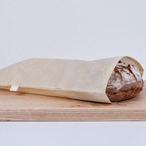 Op de afbeelding: Een brood in een beige linnen broodzak, liggend op een houten snijplank.
