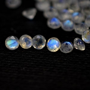 May include: A close-up of six iridescent moonstone beads, each with a round, faceted shape. The beads are arranged in a row on a black surface.